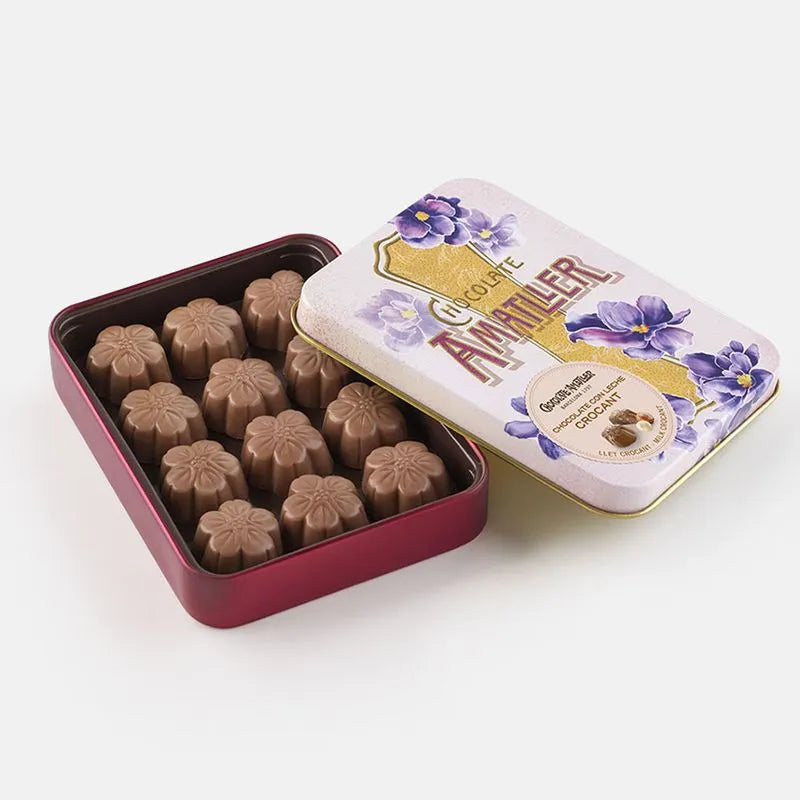 Lata metálica con decoración de flores elegantes abierta, en su interior bombones de flores de chocolate con leche crocant.
