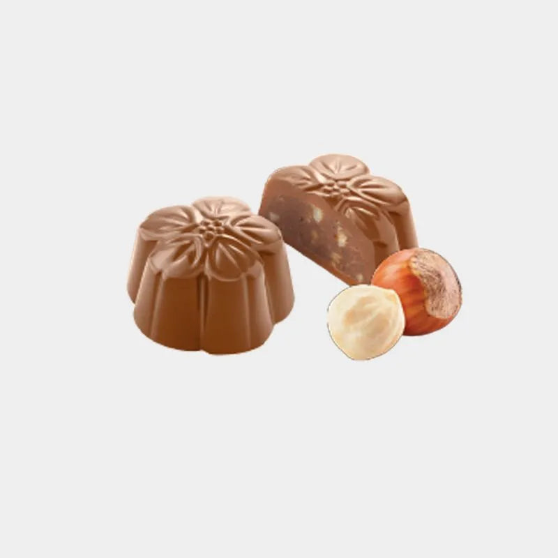 Dos bombones flor de chocolate con leche crocant. Uno de ellos podemos observar su interior cremoso con trozos de avellana.