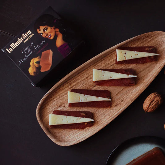 Trozos de crema de membrillo La Membrillera acompañados de cuñas de queso en una mesa junto a su caja de packaging negro.