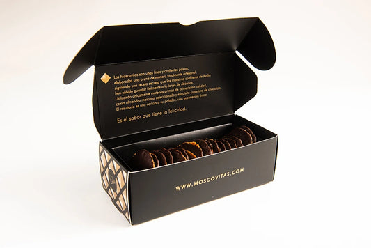 Caja negra de Moscovitas Dark abierta con la solapa levantada, mostrando en su interior las finas pastas de almendra con cobertura de chocolate cuidadosamente colocadas.
