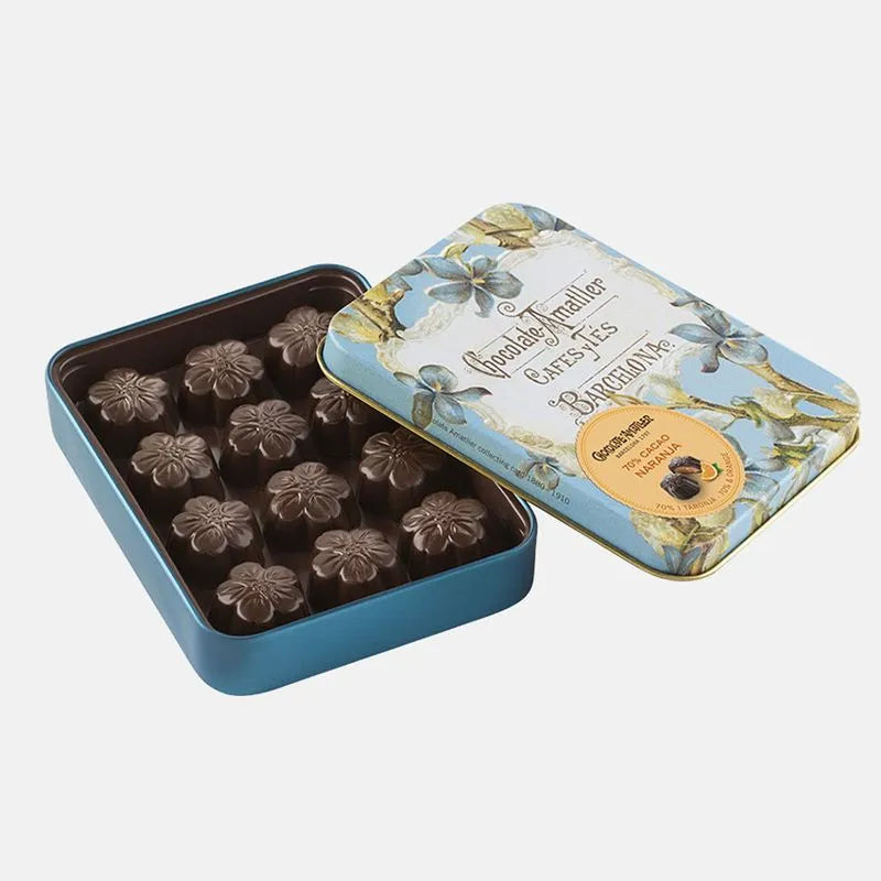 Lata abierta en su interior flores de chocolate negro rellenas de naranja. La lata metálica decorada con flores y tonos azules elegante.