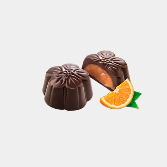 Bombones en forma de flores de chocolate negro, uno de ellos partido por la mitad para observar su relleno de naranja junto a una rodaja de naranja.