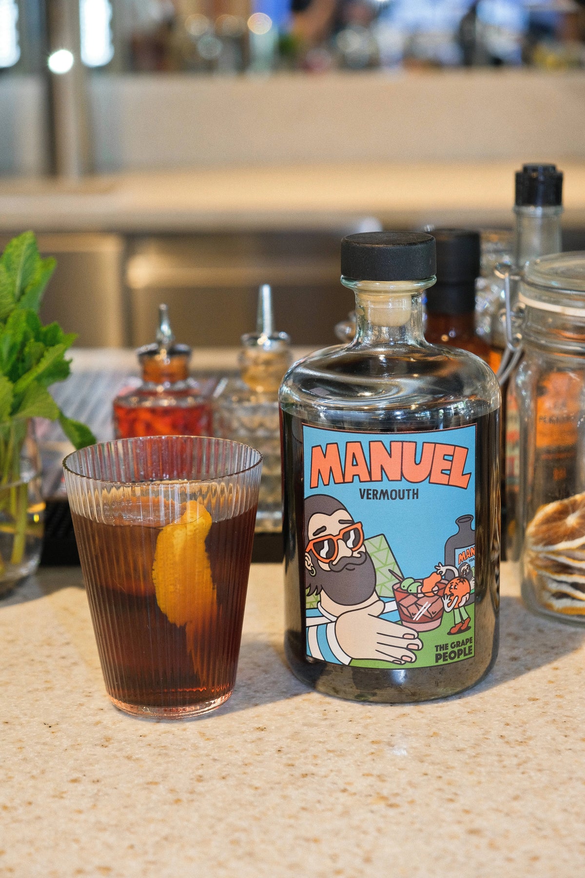 Vermouth Manuel servido en un vaso presentado junto a su botella moderna de Manuel Vermouth.
