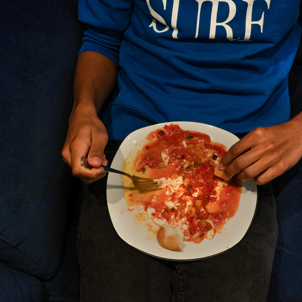 primer plano de un plato con huevos y pisto y una persona comiendo y mojando pan