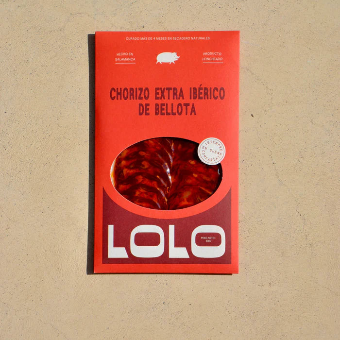 Sobre de chorizo ibérico de bellota loncheado sobre fondo marrón claro, con envase rojo, letras en rojo y la marca en blanco. Una abertura central permite ver las lonchas de chorizo en el interior.
