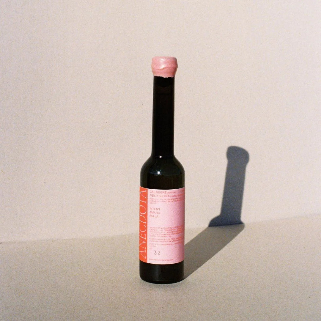 Botella de aceite de oliva virgen extra Cal Negre de Anécdota sobre fondo gris de estudio, con etiqueta y tapón de cera en tonos rosas que contrastan con la tipografía en colores rojo y rosa.
