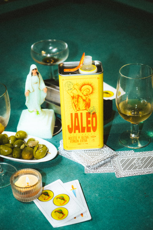 Lata de AOVE Jaleo en una mesa española con una virgen, aceitunas y cartas de la baraja