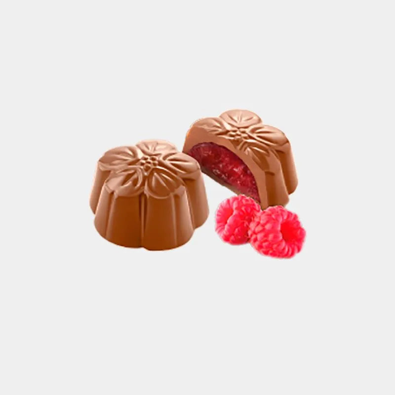 Dos bombones en forma de flor de Chocolates Amatller, uno entero mostrando su relieve floral y otro partido por la mitad dejando ver su cremoso rellenado de frambuesa, acompañados de dos frambuesas frescas en D'12 Gourmet