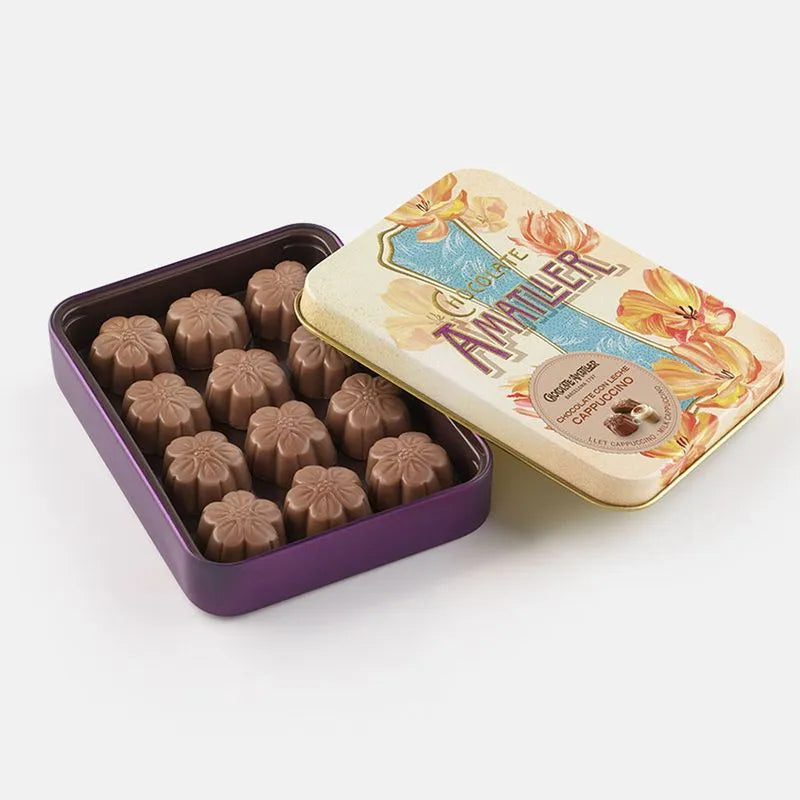 Lata de bombones de cappuccino de Chocolates Amatller sobre fondo de estudio, mostrada abierta con su elegante diseño vintage en tonos anaranjados con motivos florales, dejando ver en su interior las flores de chocolate en D'12 Gourmet