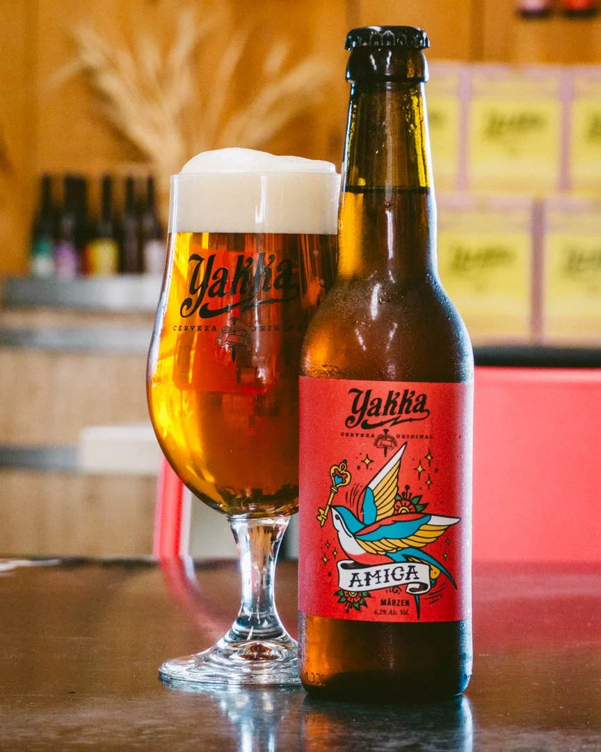 Cerveza Yakka tipo Marzen con etiqueta roja sobre una mesa de bar, acompañado de vaso con cerveza.