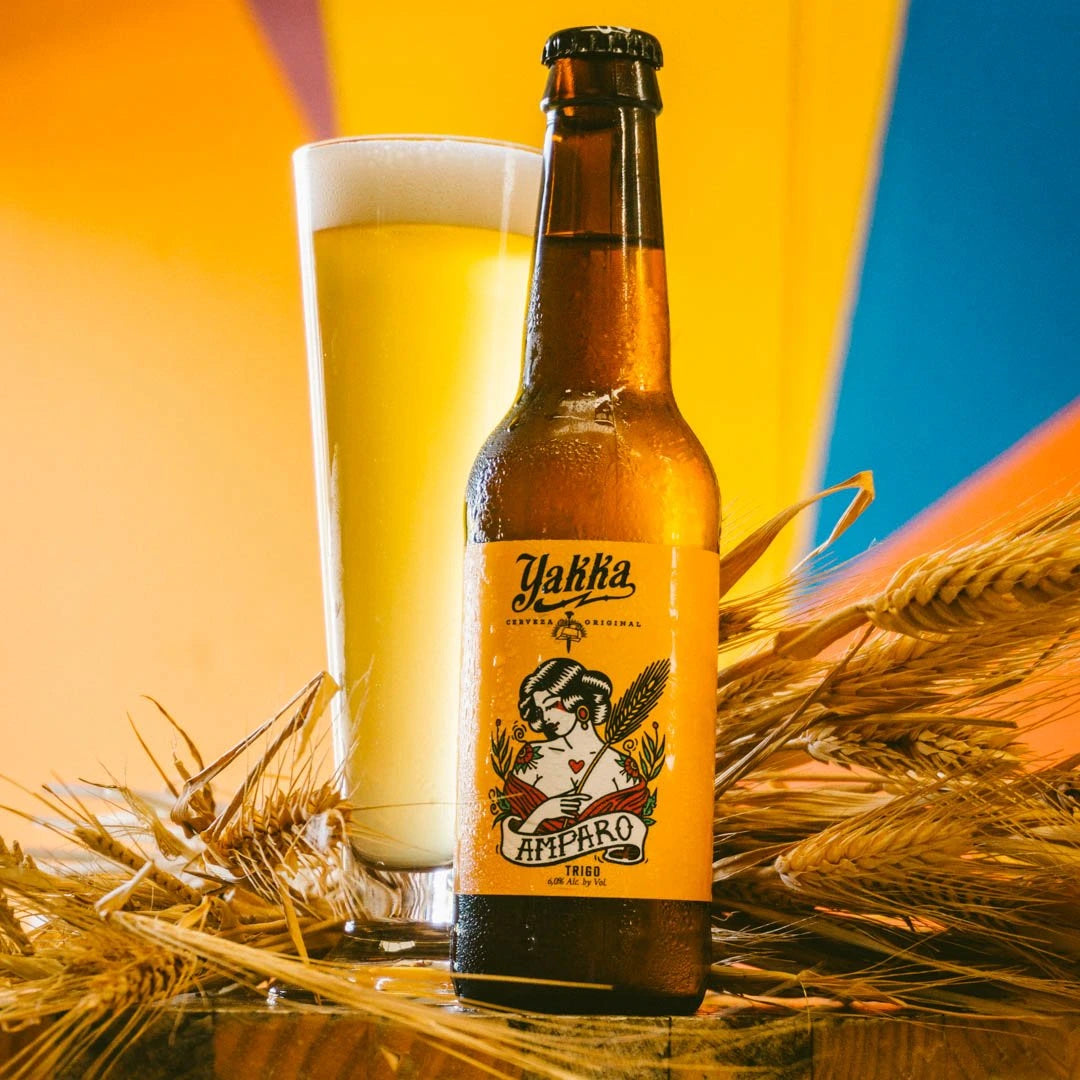 Botella de cerveza artesana de Murcia con etiqueta amarilla acompañada con su vaso sobre fondo de espigas de trigo