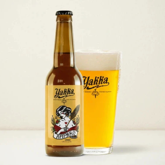 Botella de cerveza artesana de Murcia de trigo con etiqueta amarilla acompañada con su vaso sobre fondo blanco