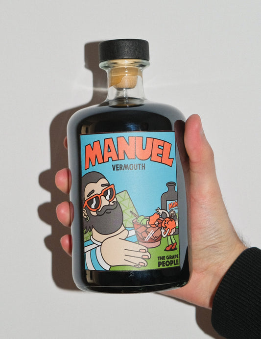 Botella de Manuel Vermouth con etiqueta moderna sostenida por una mano con fondo blanco