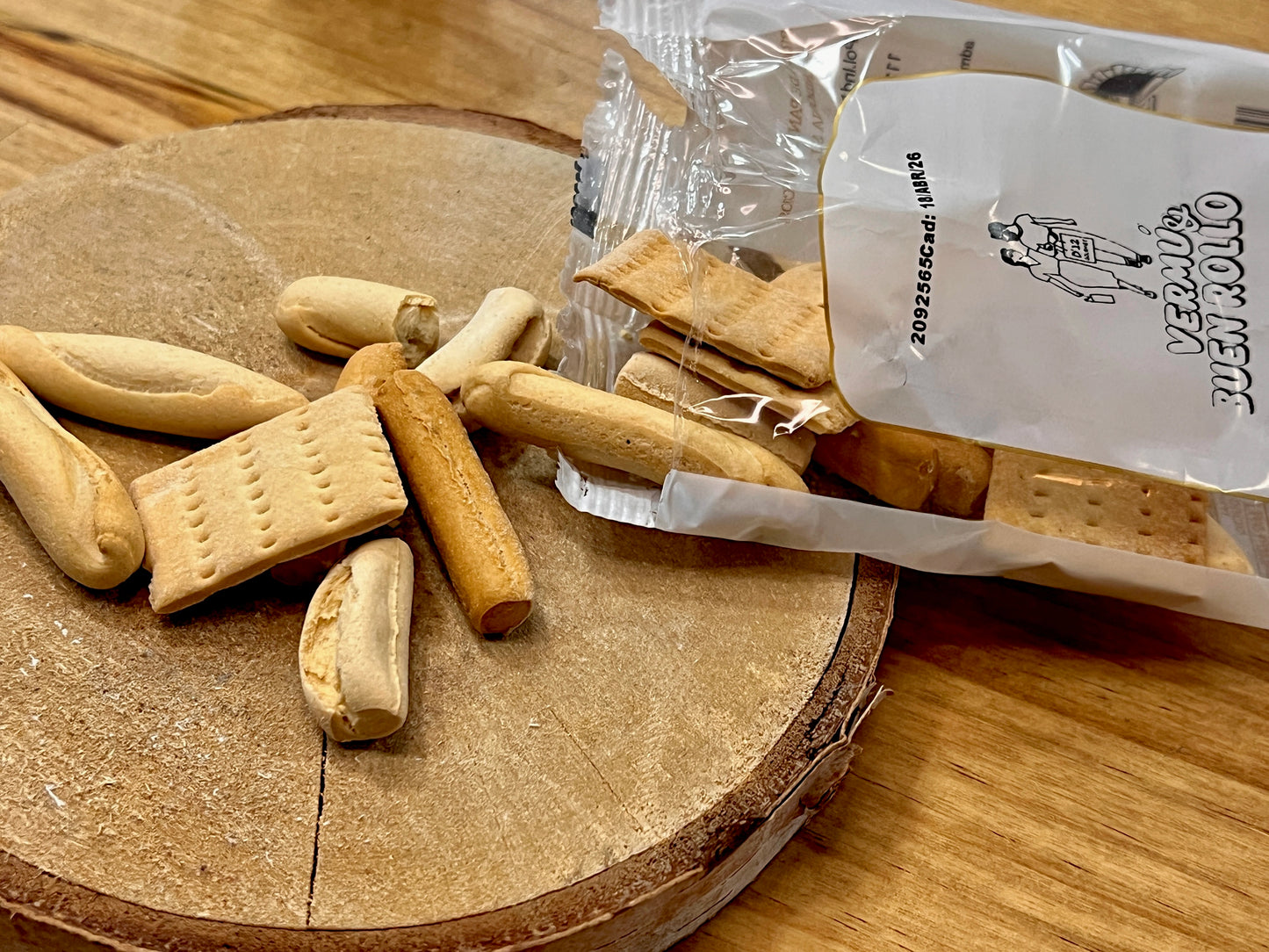 Bolsa de 25 gramos abierta donde salen de ella los panes y picos, esparcidos sobre la mesa. Se ven diferentes panes y picos artesanos saliendo de la bolsa D'12 Gourmet, Vermú&BuenRollo.