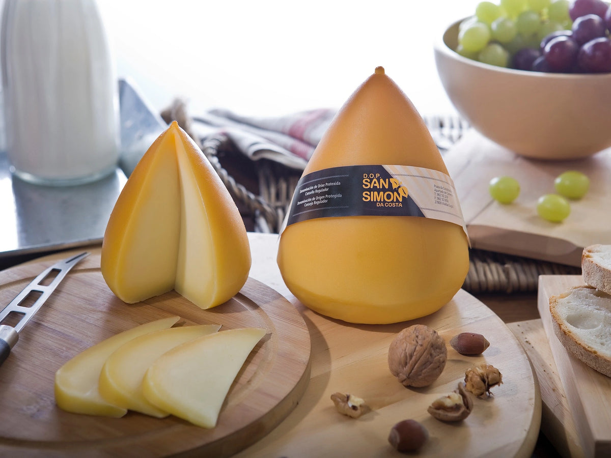 Dos piezas de queso San Simón da Costa Bufón de Don Crisanto sobre una mesa, una de ellas cortada mostrando la textura y el color de su interior.