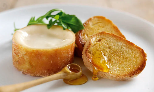 Queso cremoso de leche cruda de oveja untado en pan tostado, acompañado de miel y copa de vino.