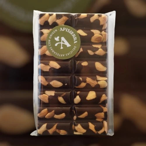Tabletón de chocolate negro con almendras enteras y tostadas a mano, y en la parte superior izquierda con una pegatina circular de color verde donde podemos ver escrito, Apisierra, delicias artesanales con origen.