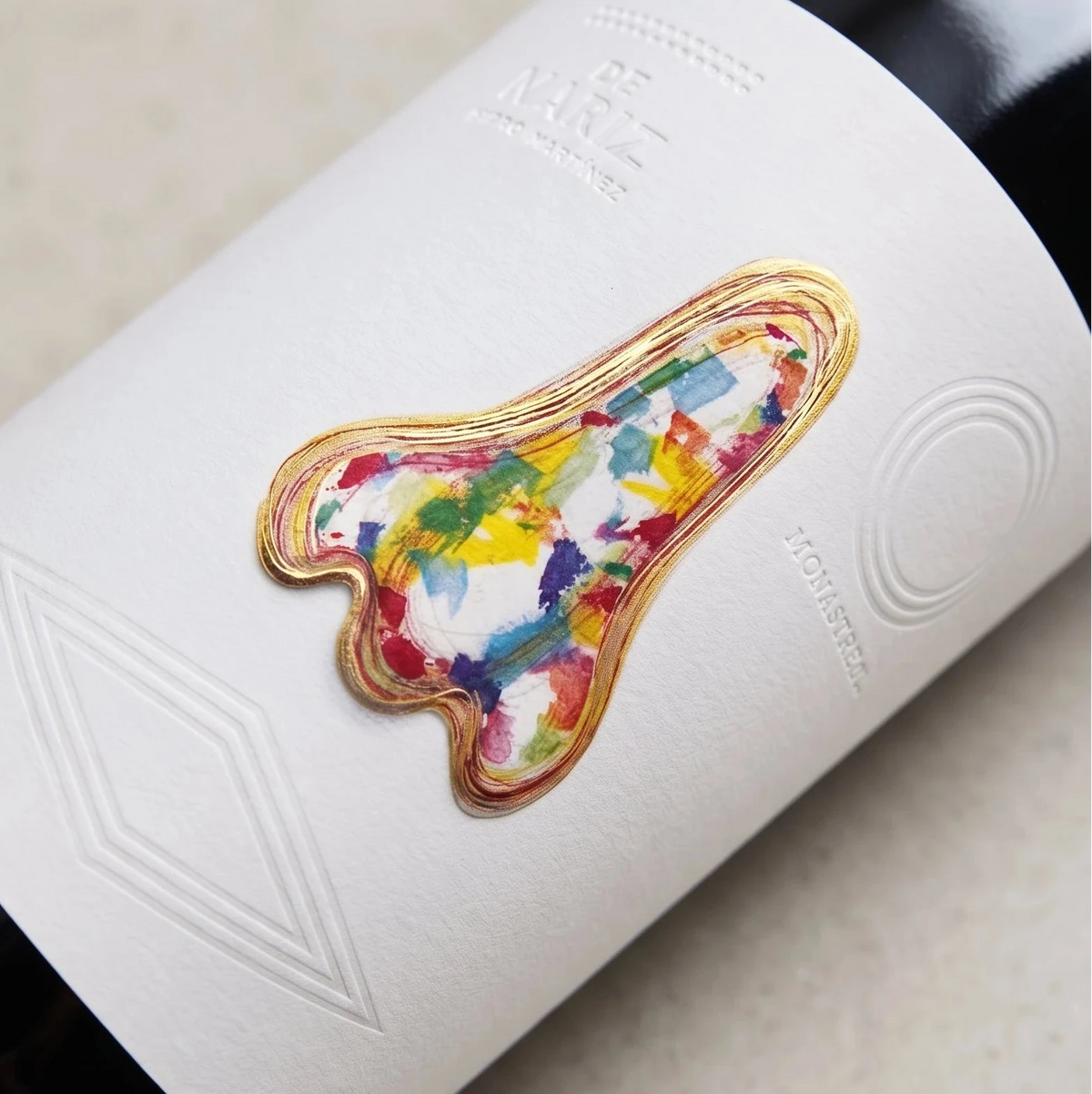 Primer plano en detalle de la etiqueta blanca del vino tinto De Nariz "La Martínez" sobre fondo de estudio, resaltando el diseño artístico de un rostro ilustrado de perfil con trazos a bolígrafo e intrincados detalles de color en su interior en D'12 Gourmet
