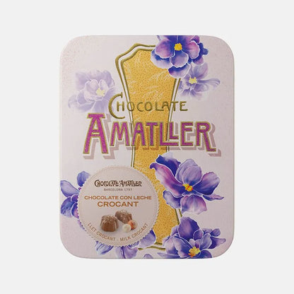 Lata metálica muy elegante con temática floral de tonos morados y amarillos. En su interior bombones en flor de chocolate con leche crocant de Chocolates Amatller.