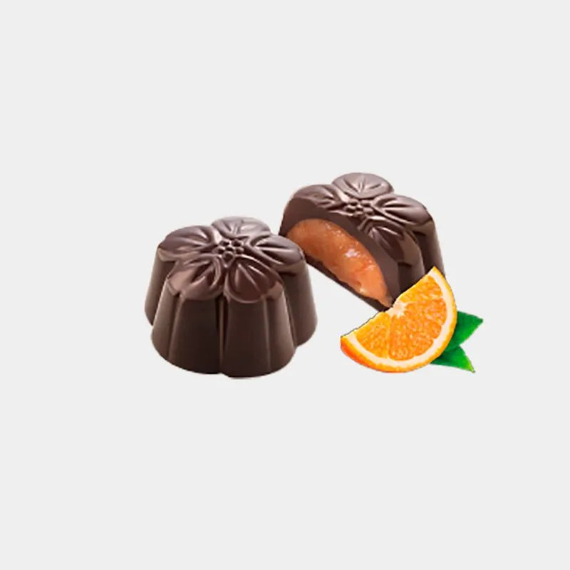 Bombones en forma de flores de chocolate negro, uno de ellos partido por la mitad para observar su relleno de naranja junto a una rodaja de naranja.