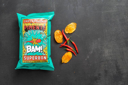 Bolsa de patatas sabor chili Superbon sobre fondo negro tipo pizarra, con envase azul de tipografía moderna y llamativa en varios colores, acompañada de tres patatas y tres chilis.