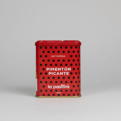 Bote rojo con puntos negros y letras en blanco, las cuales pone: Pimentón Picante La Pastora. Con tapa roja de dos tipos de aperturas, para dos tipos de calibres.
