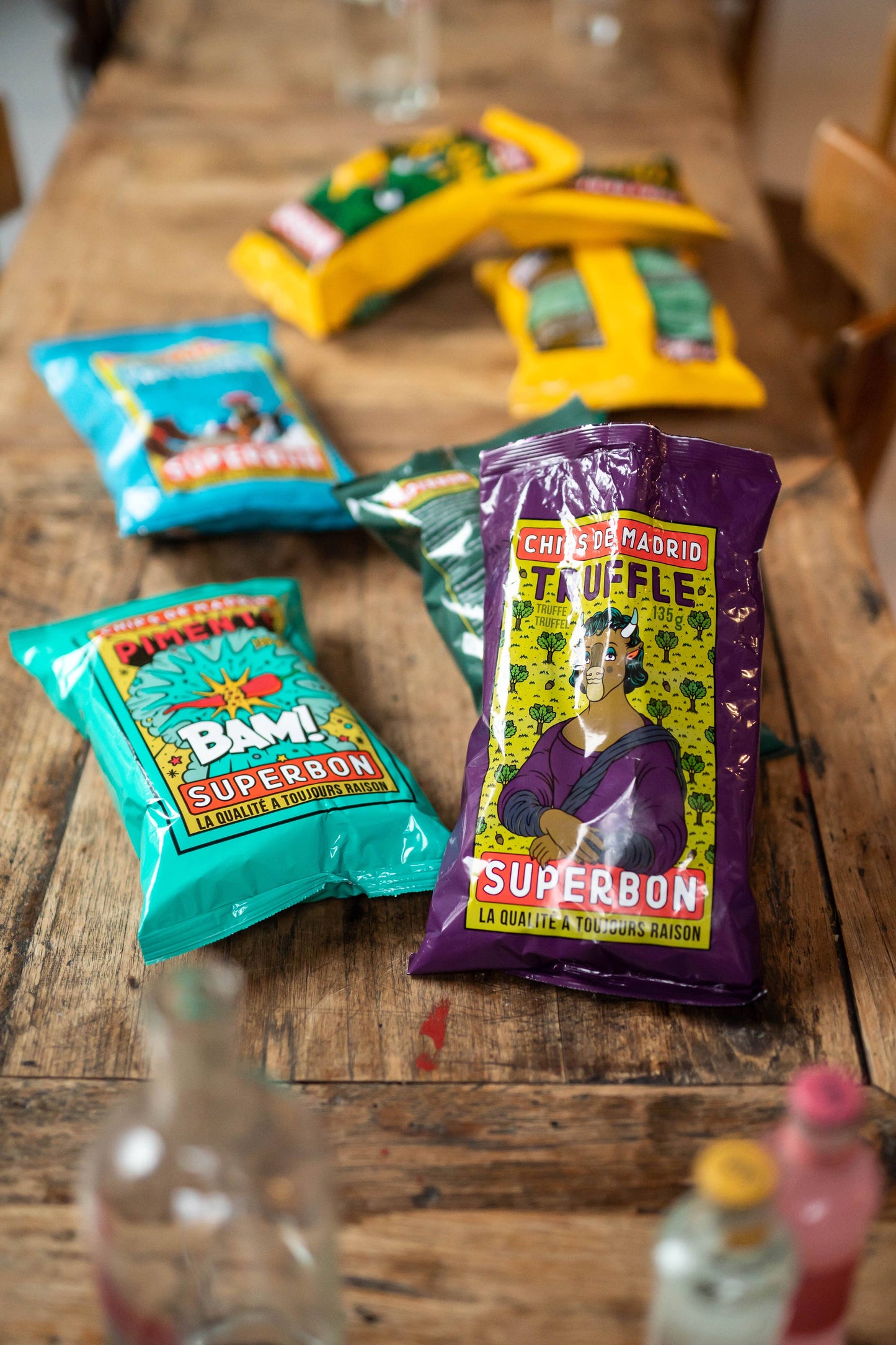Bolsas de patatas fritas Superbon sobre una mesa de madera, con las variedades de trufa y chili en primer plano y el resto de sabores desenfocados al fondo, mostrando la gama de productos de la marca.