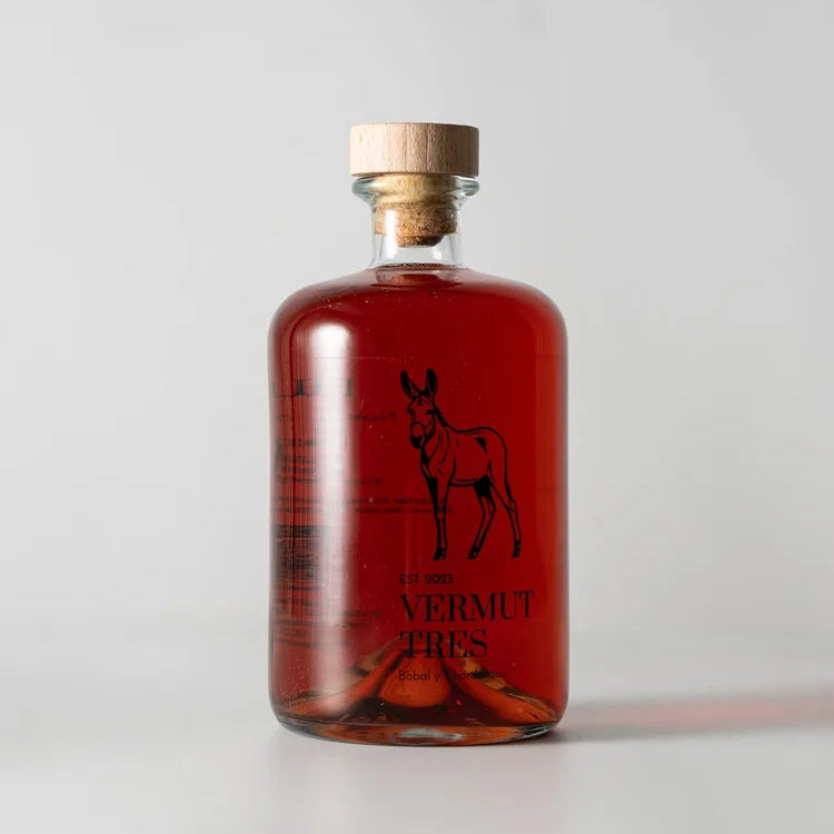 En el centro de la pantalla vermut Tres Rucio, botella de vermut rosado y en el centro un burro y debajo en letras en negro Vermut Tres.