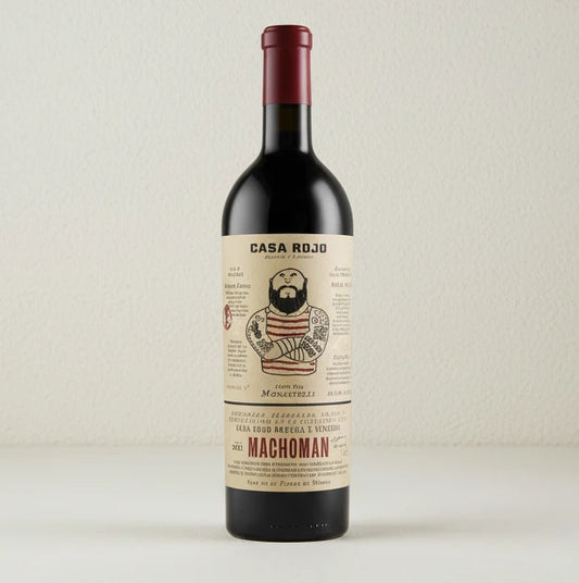 Vino tinto Machoman de la bodega Casa Rojo. Con etiqueta de color blanco crudo y en el centro el dibujo de un forzudo lleno de tatuajes. A su alrededor letras explicando el vino.