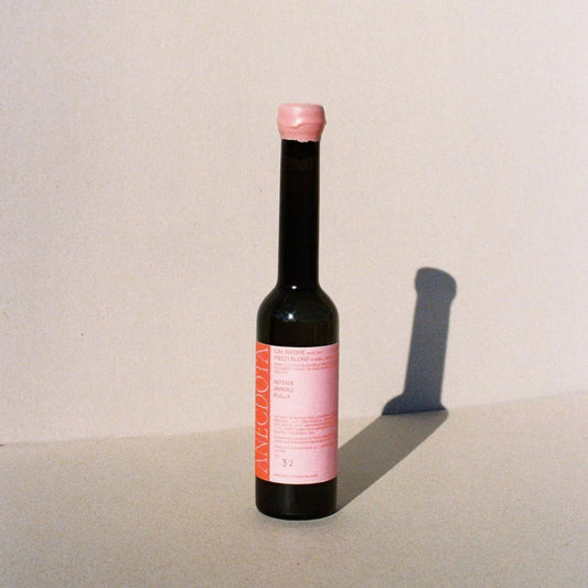 Sobre fondo gris una botella de aceite de oliva virgen extra con etiqueta y tapón de cera rosa, que contrasta con letras rojas y rosas.