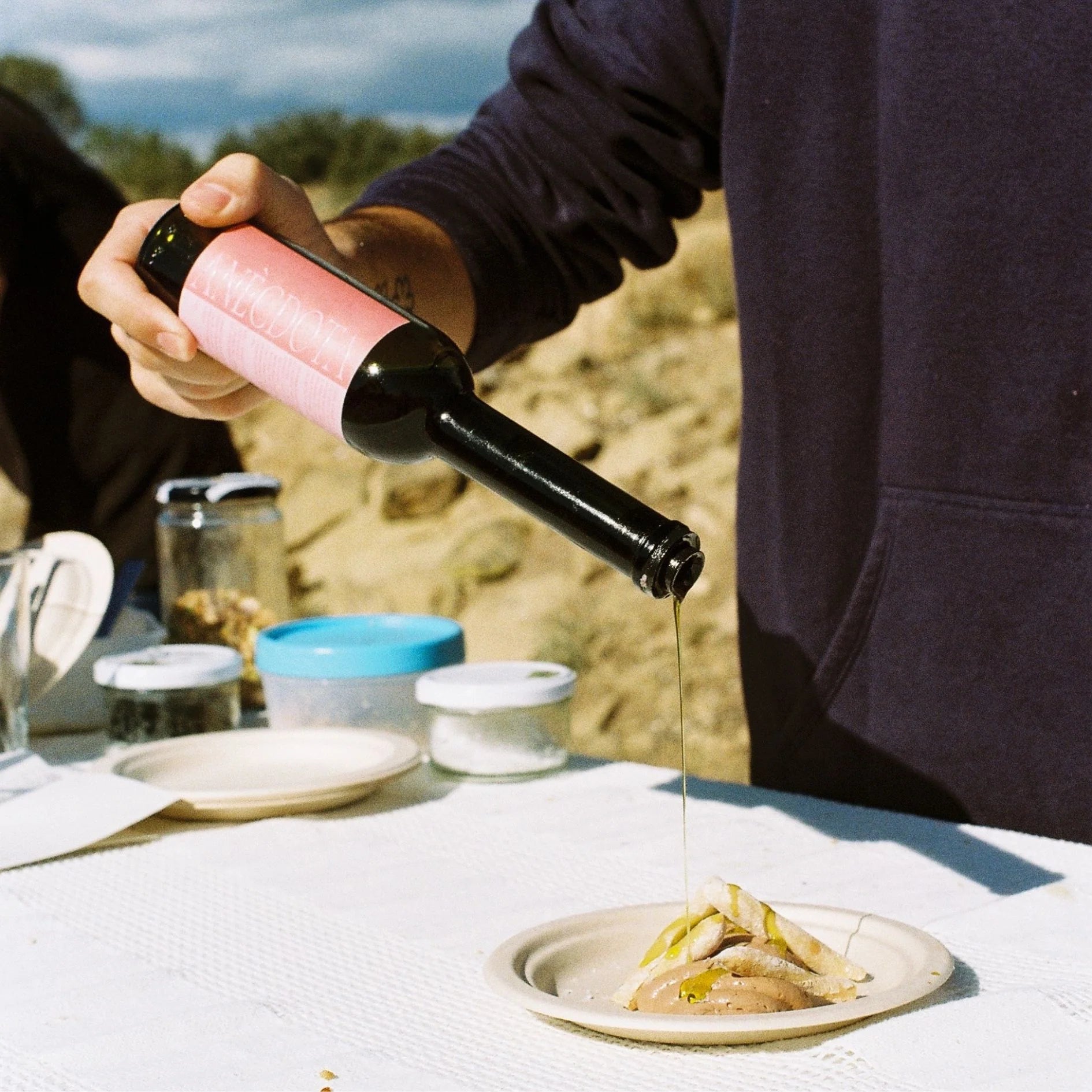Una imagen de unos campos de olivos vemos una mesa vemos como las manos de un señor vierte aceite sobre unos lomos de atún.