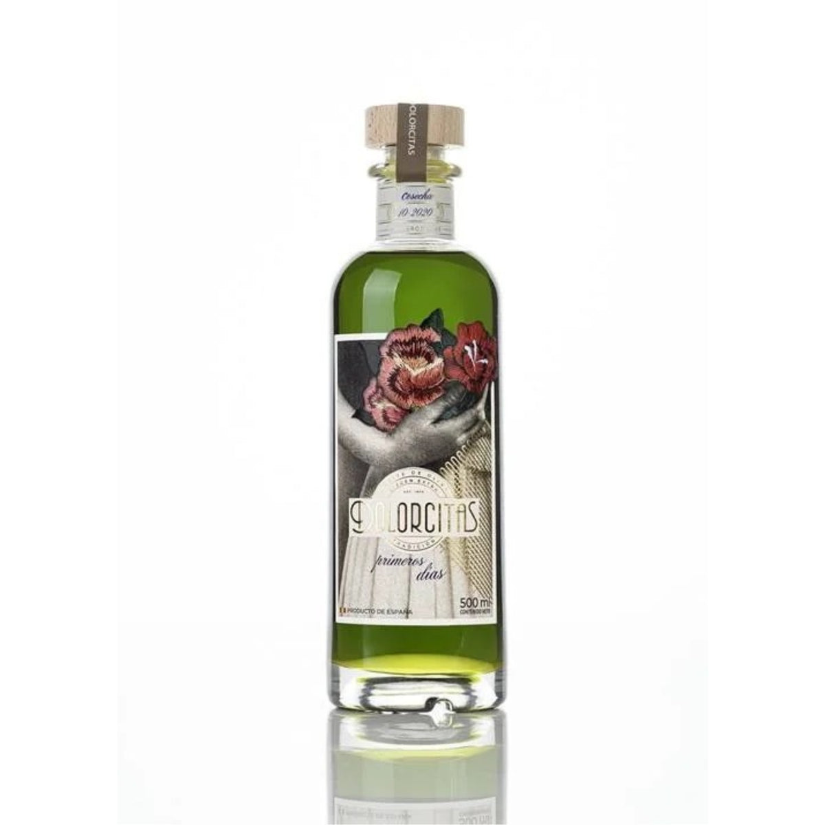 Fotografía de estudio sobre fondo neutro de la botella de aceite de oliva virgen extra Primeros Días de Dolorcitas 500ml. en D'12 Gourmet. El envase de cristal transparente permite apreciar el vibrante e intenso tono verde del aceite recién cosechado. En el frontal destaca una elegante etiqueta ilustrada con la imagen de una mujer sosteniendo un ramo de flores junto al nombre de la marca, aportando un aire refinado y artesanal.