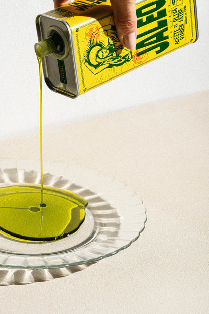 Mano vertiendo aceite de oliva virgen extra sin filtrar Jaleo desde la lata sobre un plato, mostrando el flujo, la textura y el característico tono dorado del aceite en D'12 Gourmet