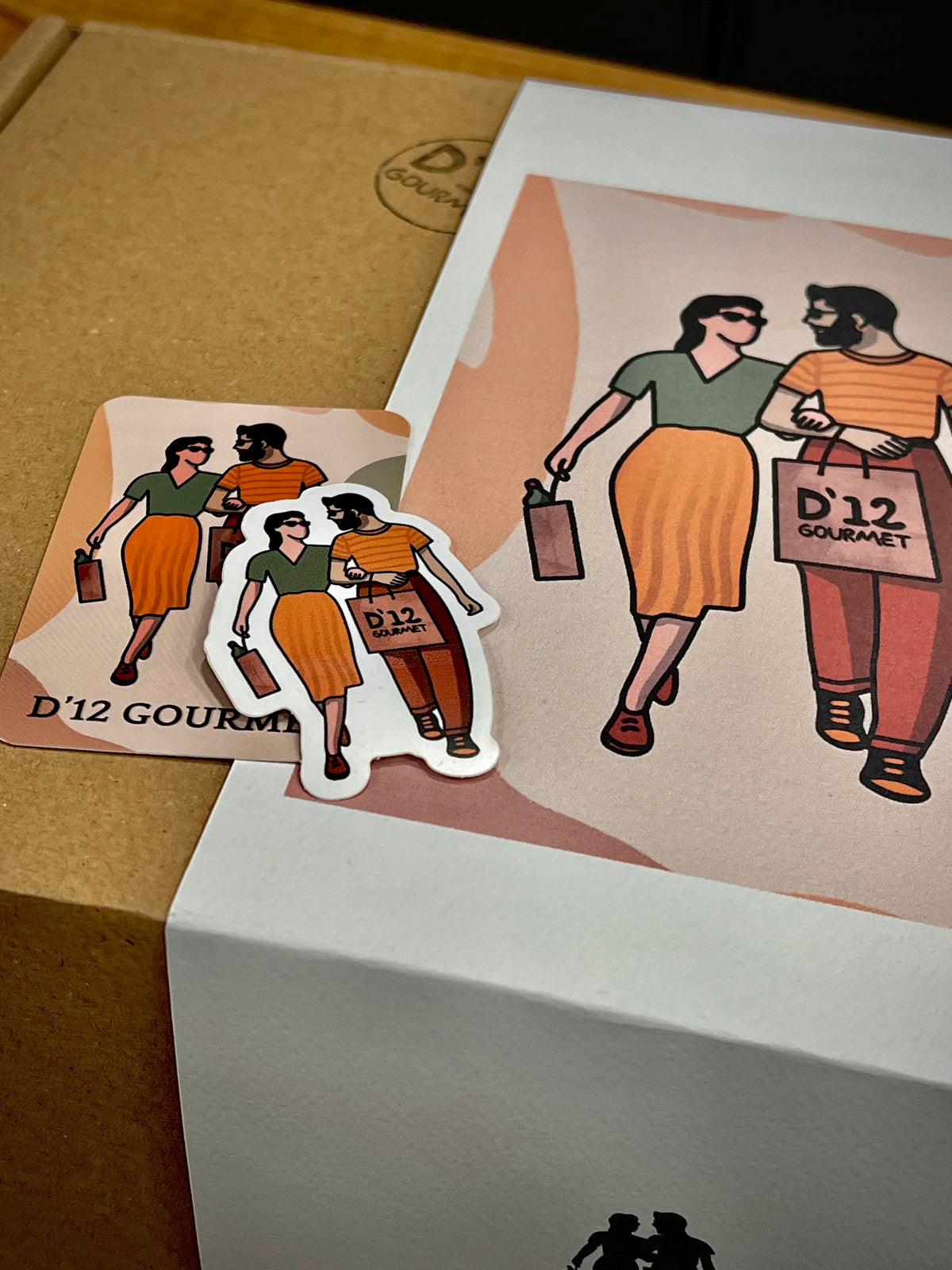 Caja especial para regalo de D'12 Gourmet. Caja de cartón con faja con el diseño de D'12 Gourmet, sobre esta caja también vemos una tarjeta y pegatina del logo del D12.