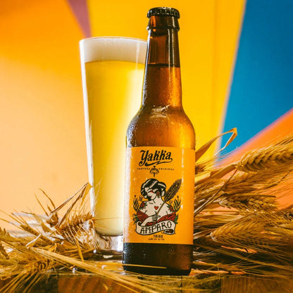 Botella de cerveza artesana de Murcia con etiqueta amarilla acompañada con su vaso sobre fondo de espigas de trigo