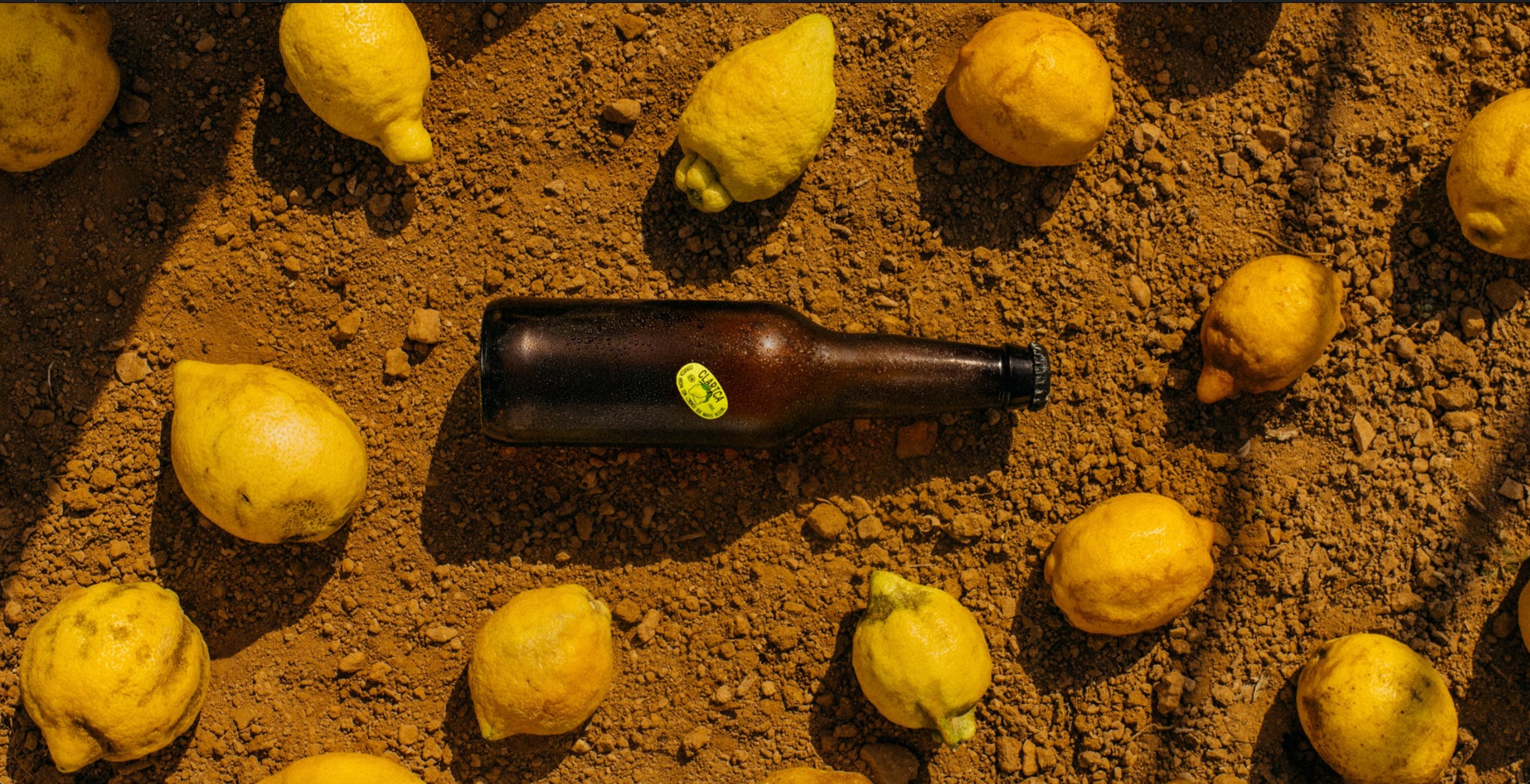Botella de cerveza en un suelo de arena rodeada de limones 