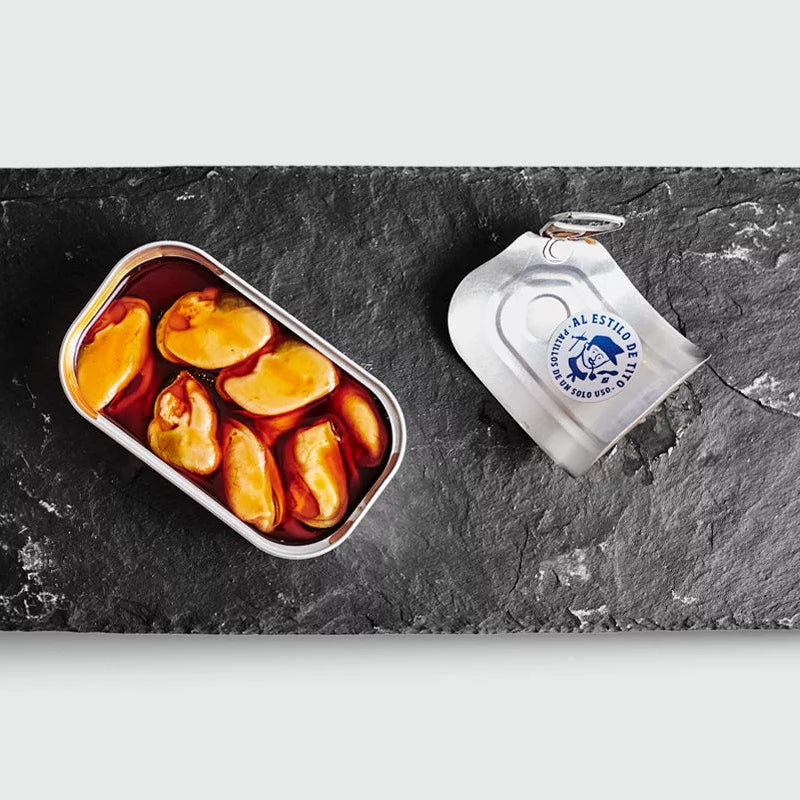 Plato de pizarra y sobre este una lata abierta de mejillones en escabeche de tamaño grande.