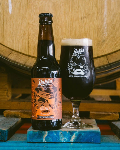 Cerveza artesana Yakka edición especial por su XVII aniversario. De etiqueta con tonos anaranjados y marrón con una caja de pirata. Junto a una copa de su propia cerveza.