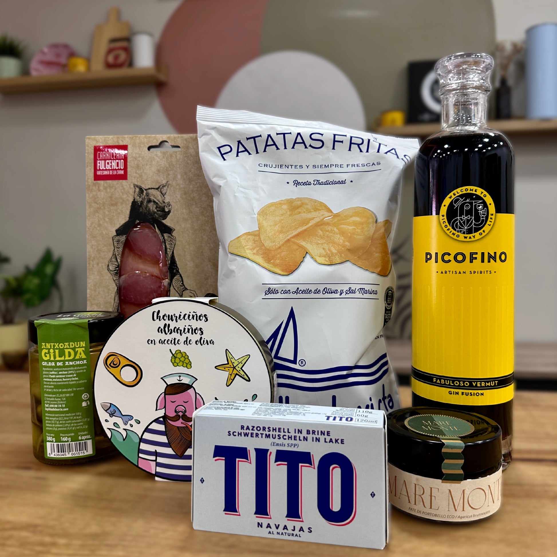 Pack pensando para un padre que se sale de la norma y le encanta el aperitivo en familia. Sobre una mesa de madera vemos un Vermut Picofino, junto a bolsa de patatas bonilla. Un sobre de jamón de Fulgencio de Lomo de chato murciano, unas gildas, chouriciño, navajas al natural y paté de portobello.