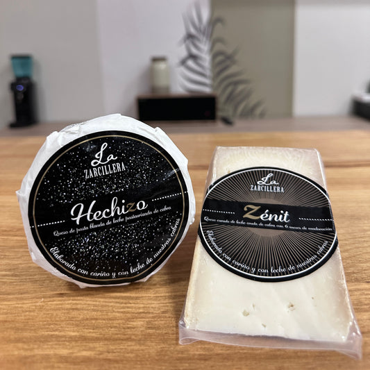Dos quesos sobre una mesa de madera, por un lado queso Hechizo, el mejor queso de cabra del 2025 junto a su hermano curado el Zenit. Ambos quesos en cuña perfecto para compartir.