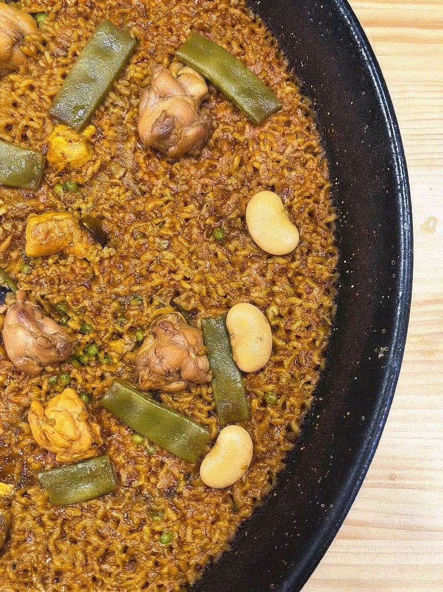 Fotografía cenital de media paellera con arroz D.O. Calasparra recién cocinado, acompañado de tiernos trozos de pollo, judías verdes y garrafón, en D'12 Gourmet