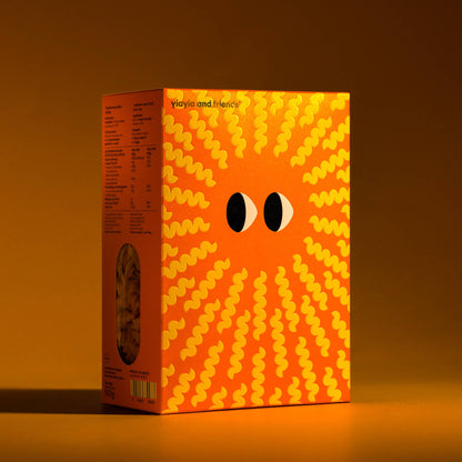 Caja de pasta Fusilli de Yiayia & Friends de perfil con paquete marrón, diseño de sol en hélice con ojos de Yiayia y ventana lateral que muestra el interior en D'12 Gourmet