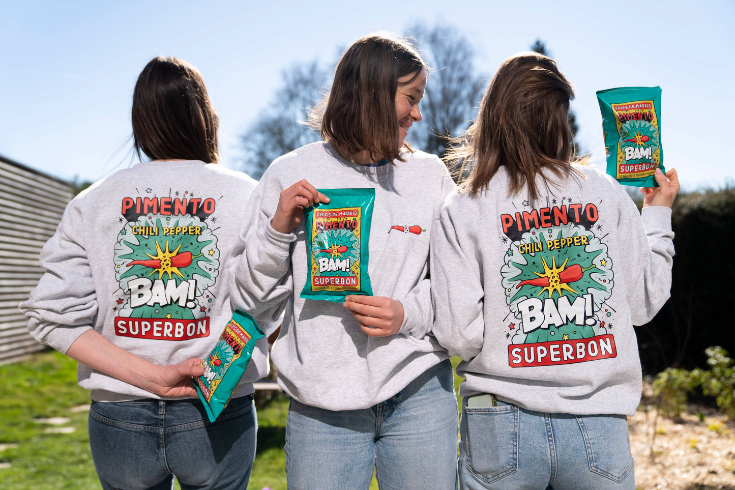 Tres chicas dos de espaldas y una de enfrente con sudaderas de las patatas fritas con chilli de superbón. Además en sus manos sostienes las propias bolsas de patatas.