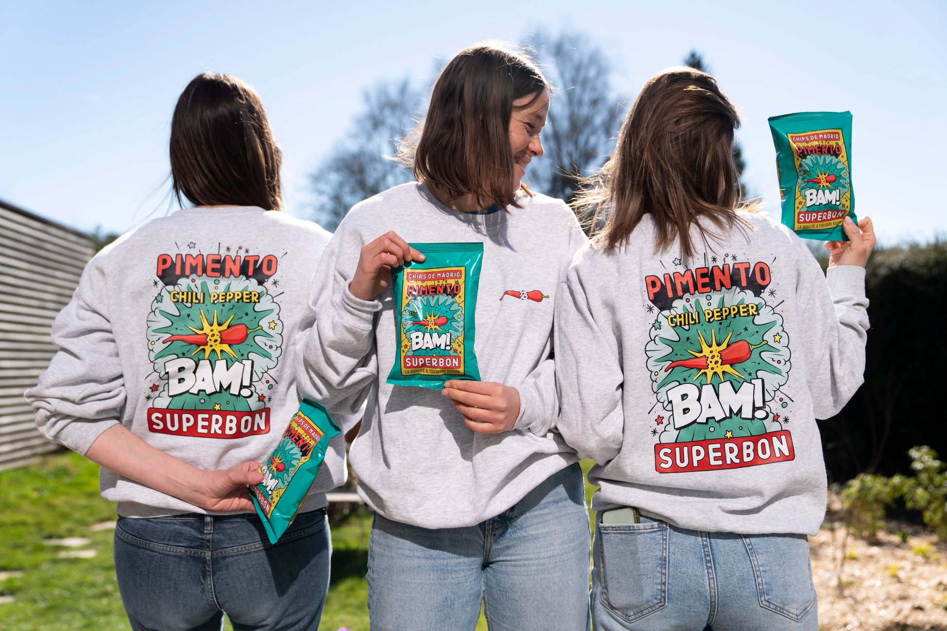 Tres chicas dos de espaldas y una de enfrente con sudaderas de las patatas fritas con chilli de superbón. Además en sus manos sostienes las propias bolsas de patatas.