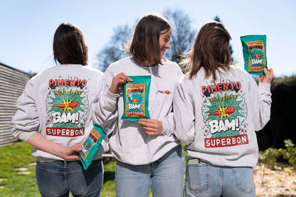 Tres chicas dos de espaldas y una de enfrente con sudaderas de las patatas fritas con chilli de superbón. Además en sus manos sostienes las propias bolsas de patatas.