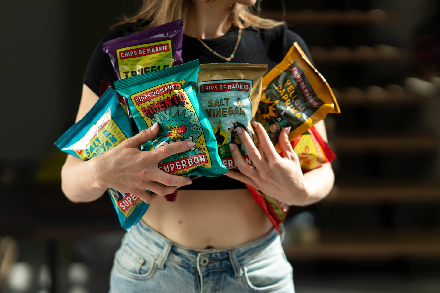 Mujer sosteniendo entre sus brazos diferentes bolsas de patatas fritas de la marca superbon.