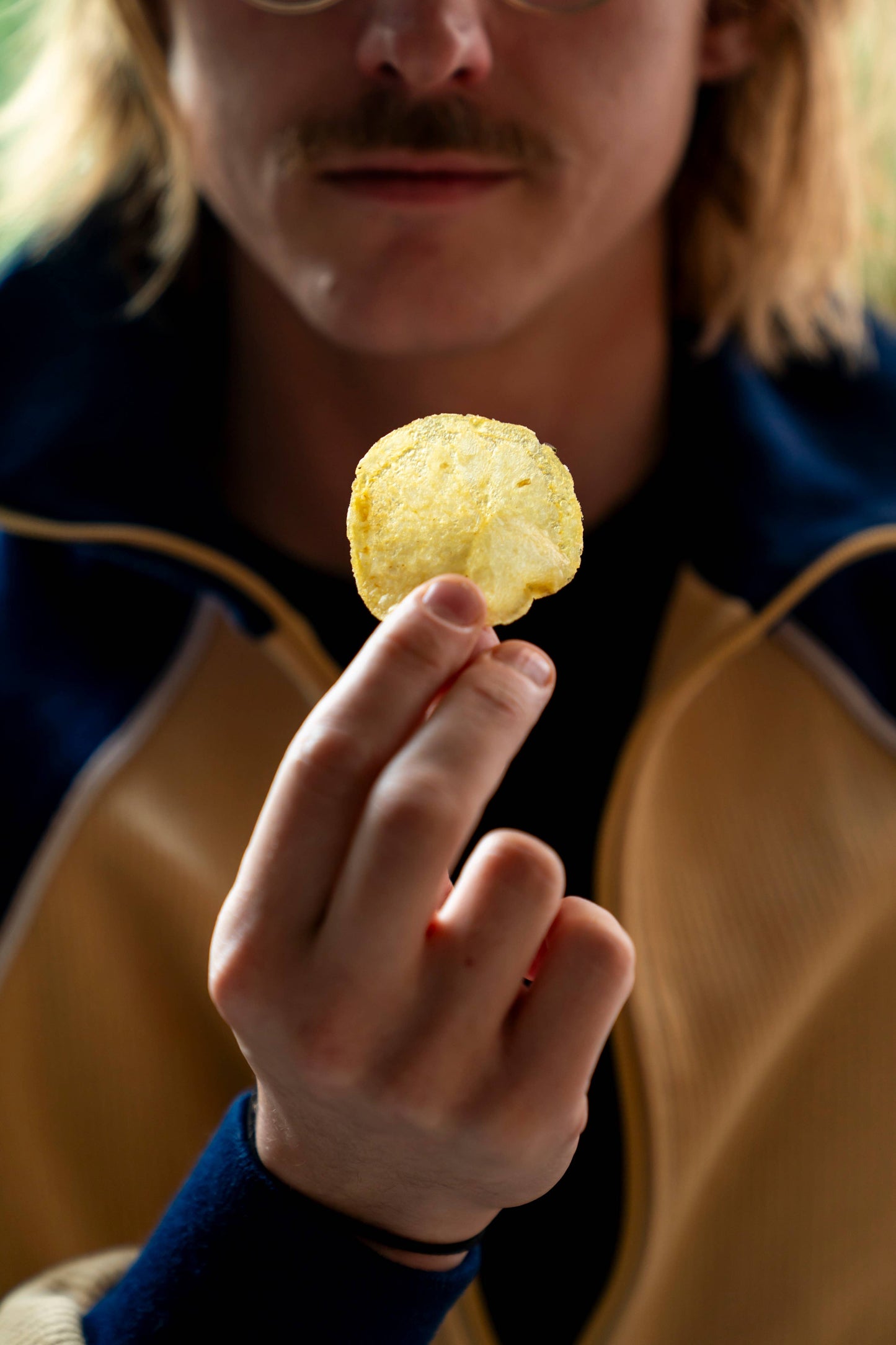 Primer plano de un hombre mostrando una patata frita Superbon entre los dedos, con parte de su rostro visible y la patata destacando por su color dorado y su textura.