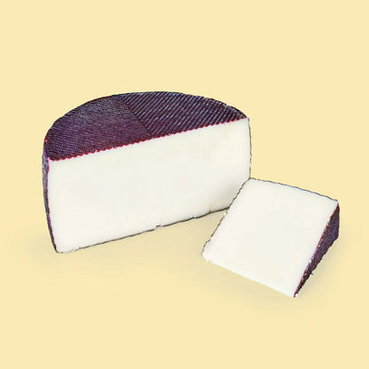 sobre fondo amarillo, medio queso de queso cerrón al vino junto a una cuña, donde podemos observar el exterior del queso y el interior.