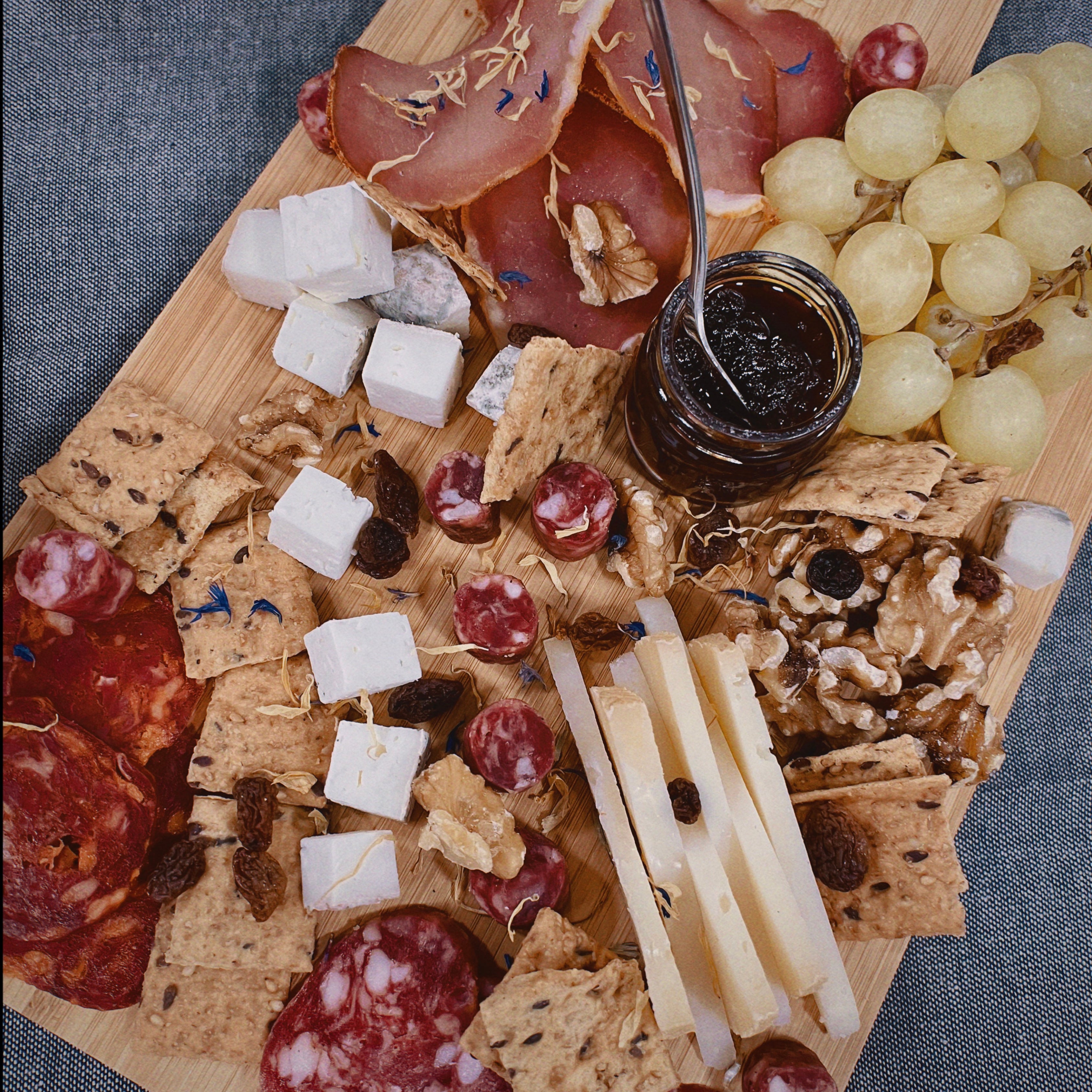 Tabla mixta de quesos y embutidos con crackers, uvas y mermelada sobre un mantel gris