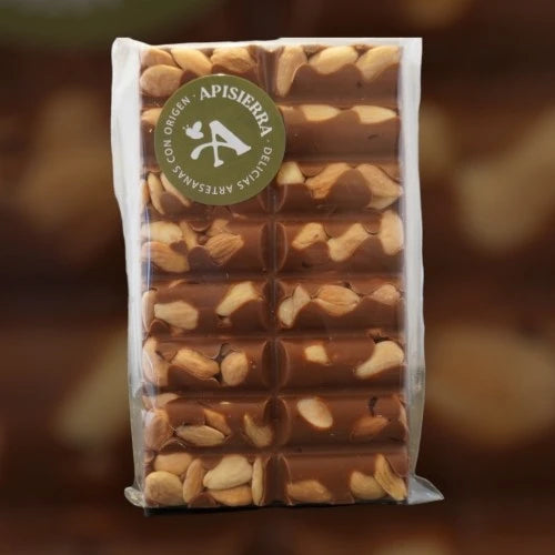 Tabletón de chocolate con leche caramelo y almendras enteras tostadas a mano, con pegatina circular verde donde pone Apisierra delicias artesanales con origen.